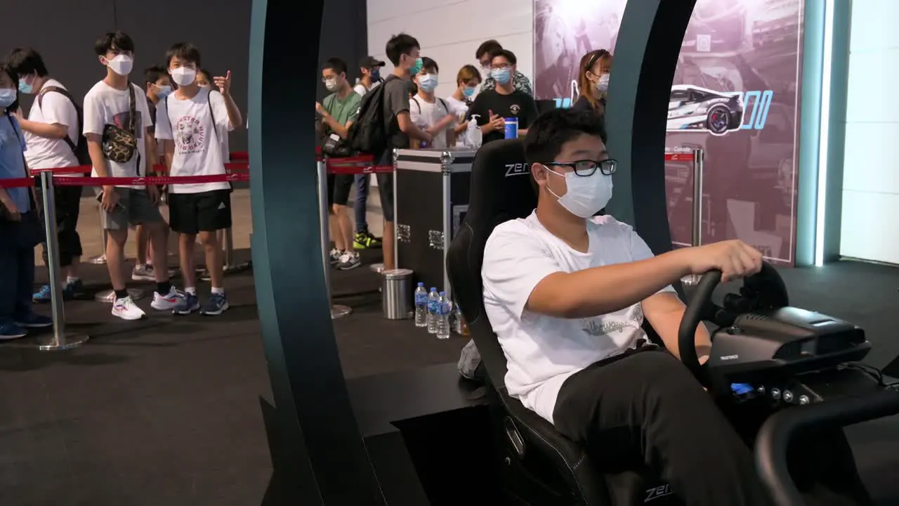 A Chinese gamer plays a themed racing videogame as visitors and enthusiasts wait for their turn during the Hong Kong Computer and Communications Festival in Hong Kong