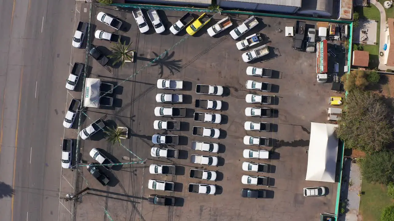 Aerial bird's eye descending spiral shot of trucks lined up at a used automotive dealership lot