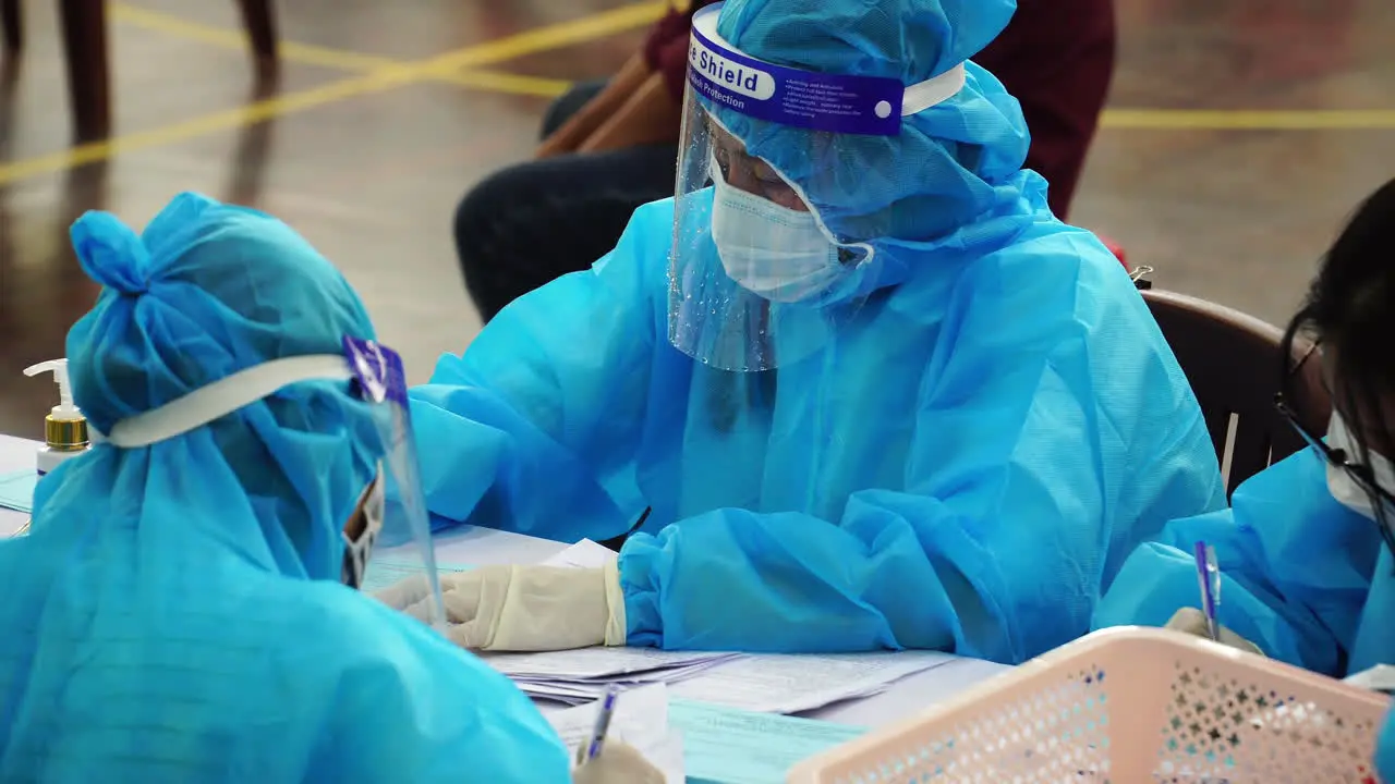 Close-up of personnel seen wearing protective suits in a vaccination hub