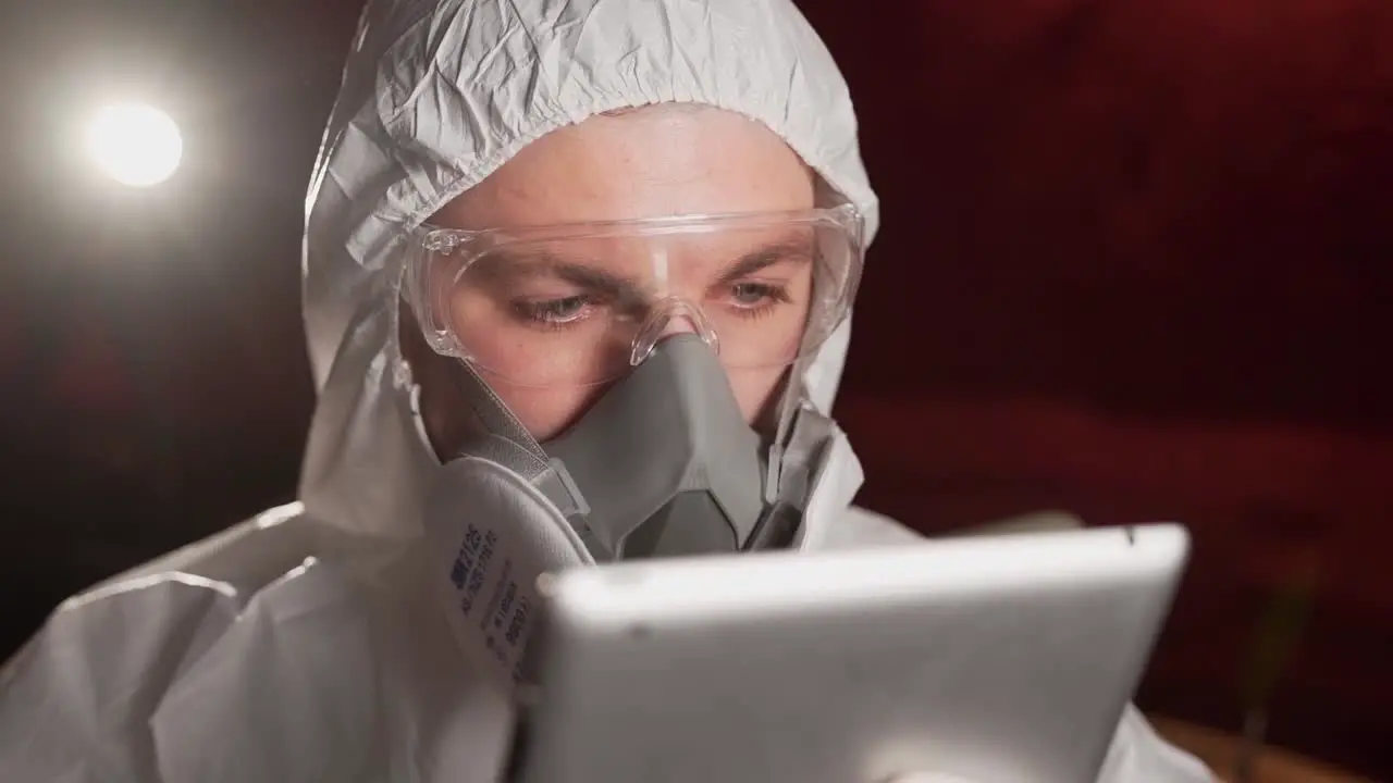 man in protective suit and mask watching news video about epidemic on tablet