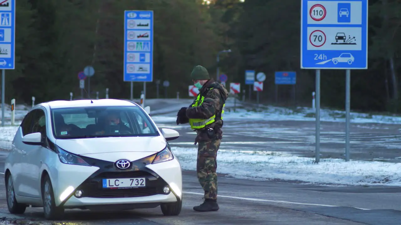 Lithuanian border guard officer control white passenger car at the Lithuania Latvia border during crisis measures in the fight against the novel coronavirus Covid-19 medium shot from a distance