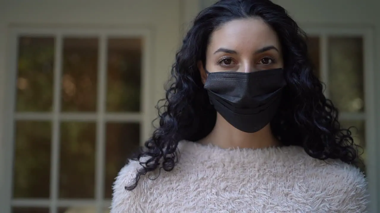 Beautiful young Latina woman wearing a black face mask and looking directly at the camera