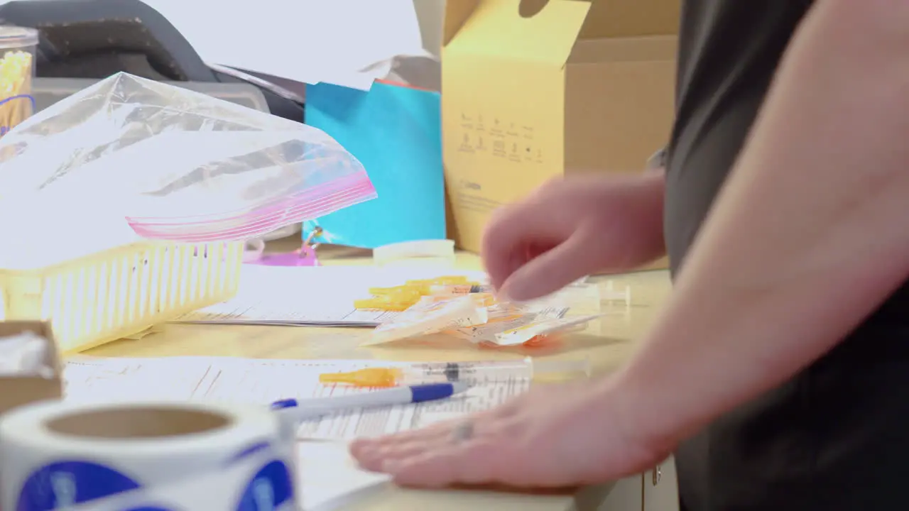 Nurse Prepares to Administer the COVID 19 Shot or Corona Virus Vaccine Injection by Gathering Clean Syringe Needles and Filled Out Paper Work in Medical Doctor’s Office with No Faces