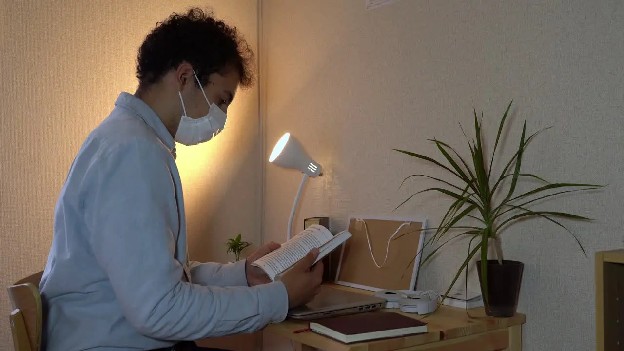 A Man Wearing Facemask Reading A Book At His Home Office During The Coronavirus Outbreak Closeup Shot