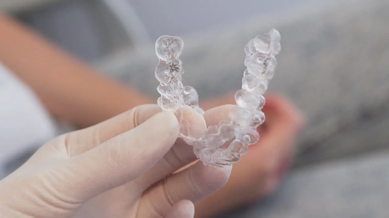 tight close-up of gloved hand holding two invisalign aligners with patient in the background