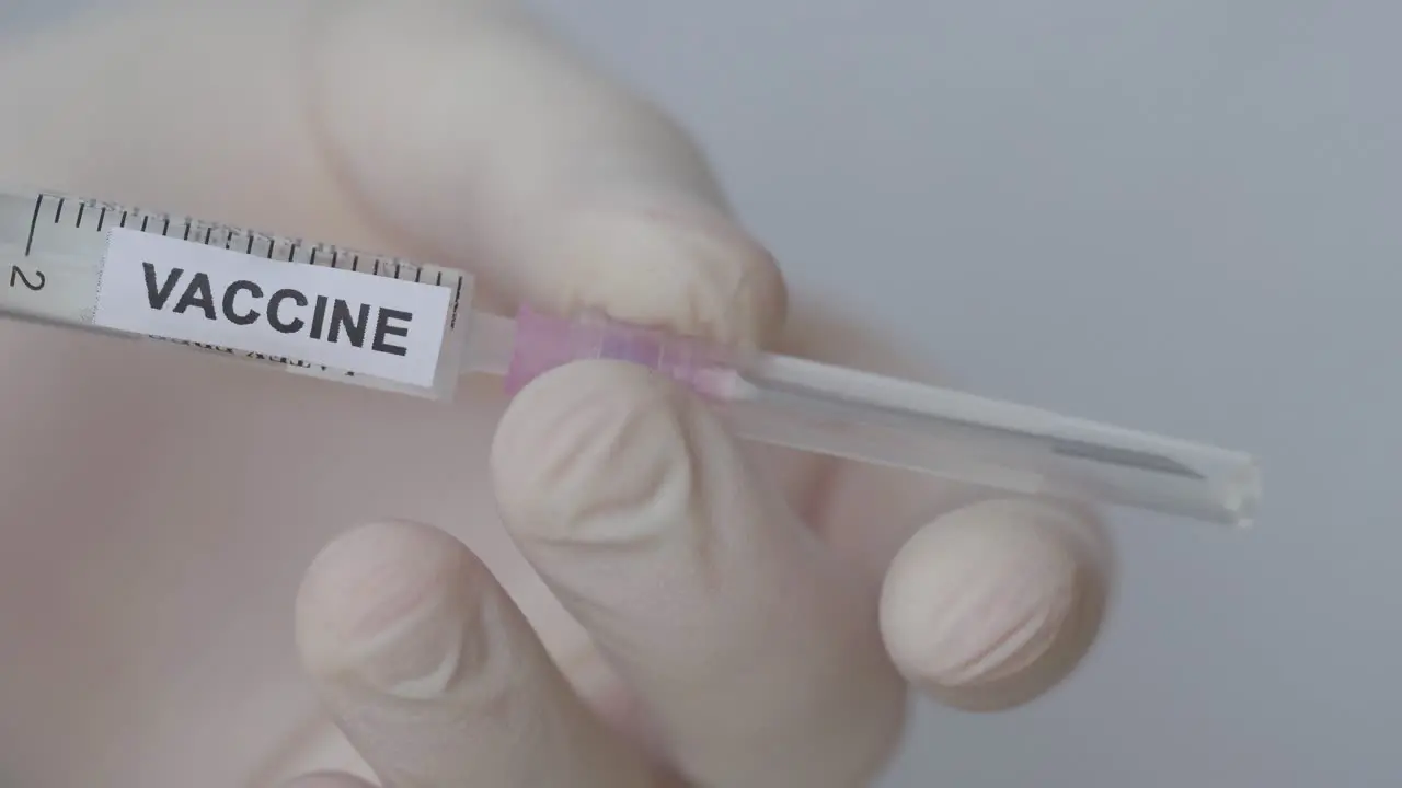 Hand With Glove Removes The Needle With Cap Of Syringe COVID-19 Vaccine