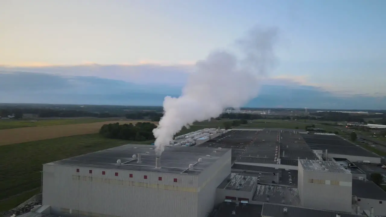 Aerial orbit of a factory with steam rising from pipe with beautiful a beautiful sunset in the background