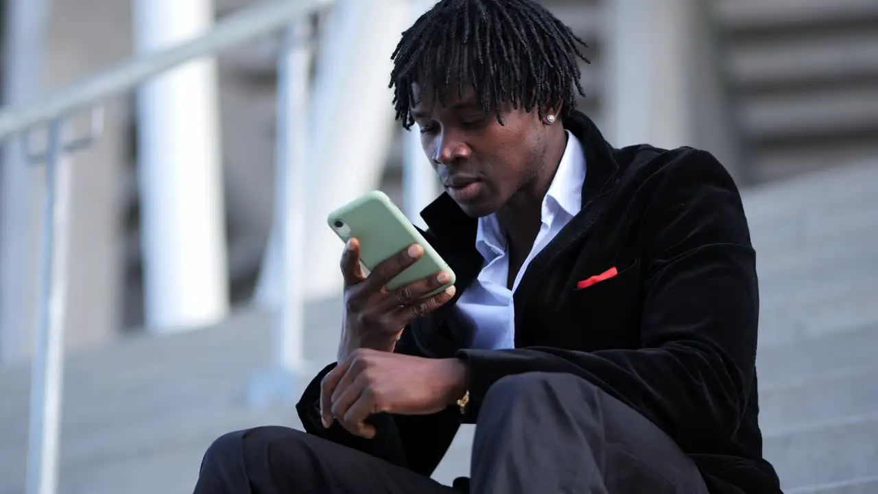 Young African Businessman in a Black Suit Recording a Voice Message on Stairs