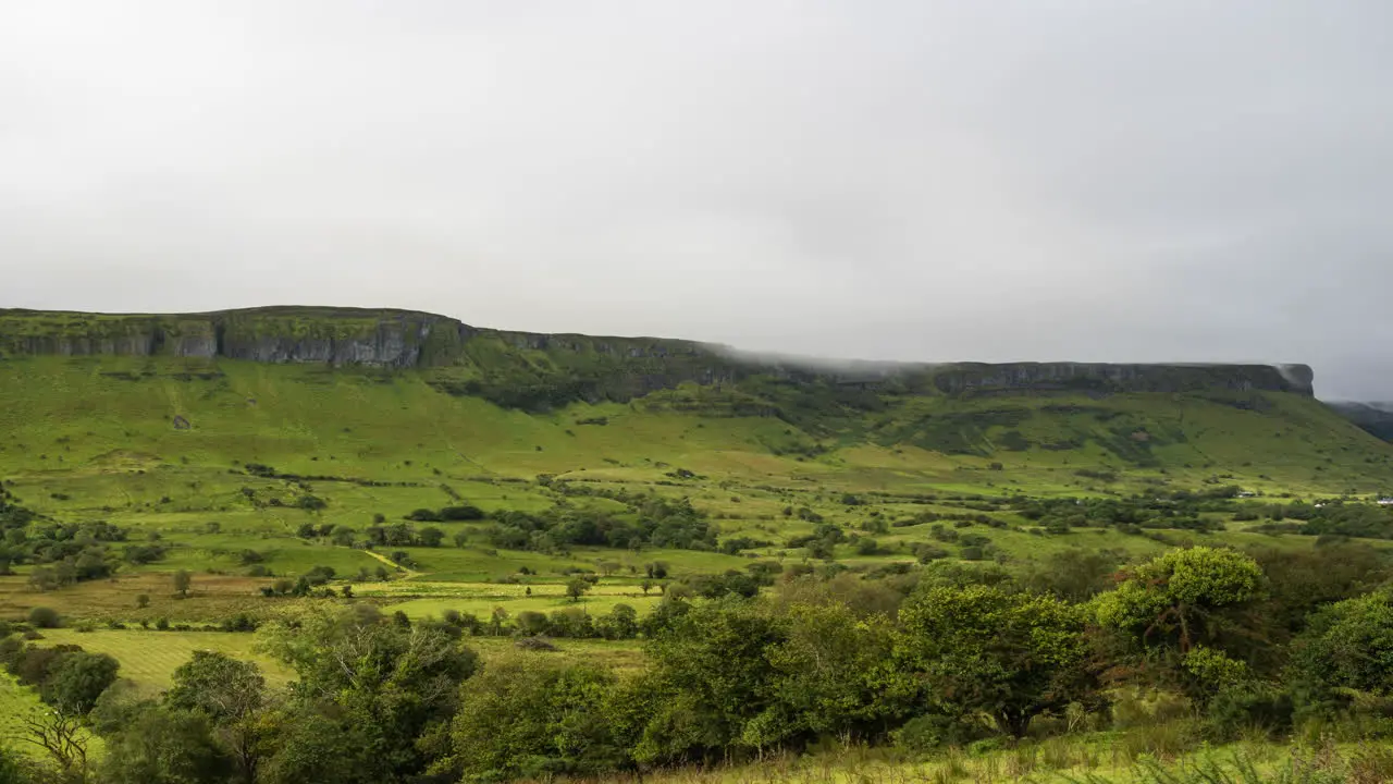 Time lapse of morning mist rolling over the green hills above and tree landscape in the foreground in rural countryside of Ireland