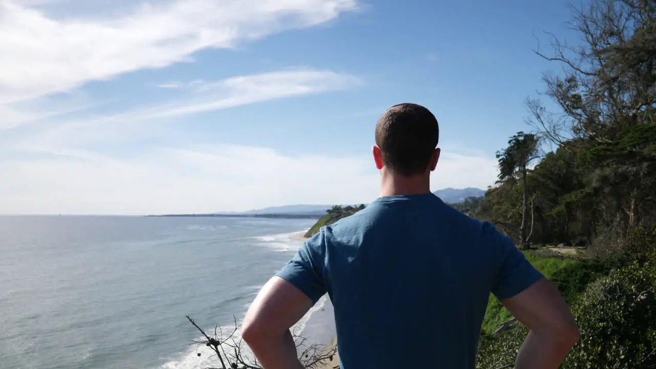 A fit strong man standing proud after a successful climb on the edge of an ocean cliff nature hiking trail in Santa Barbara California SLOW MOTION