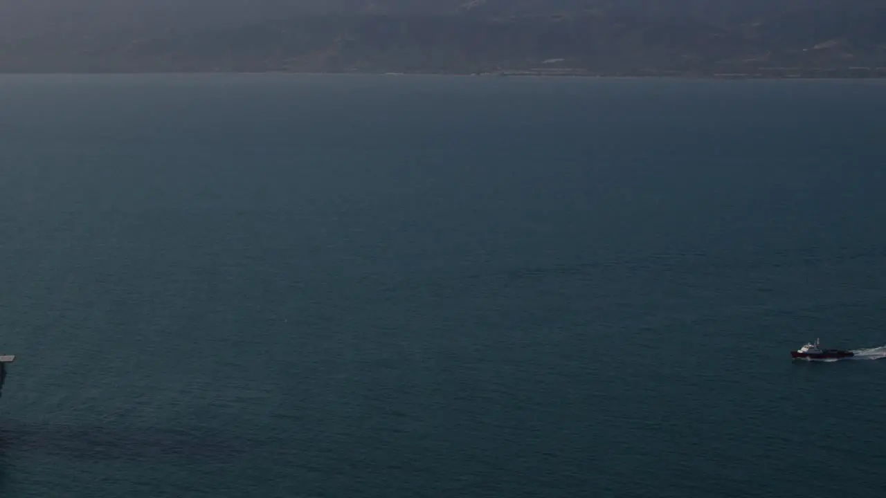 An aerial shot over a boat heading out to oil derricks and platforms in the Santa Barbara Channel California