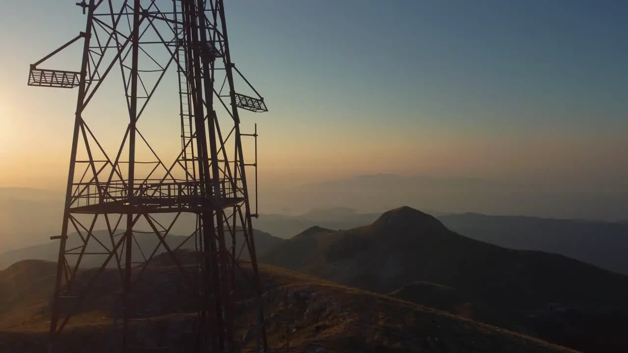 Aerial pan of the silhouette of a telecommunications tower on a mountain peak at sunrise