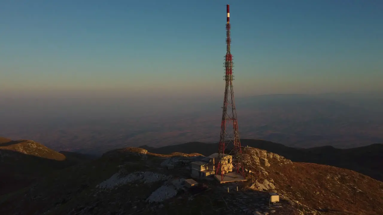 Aerial approaching large telecommunications tower on a mountain peak at sunrise