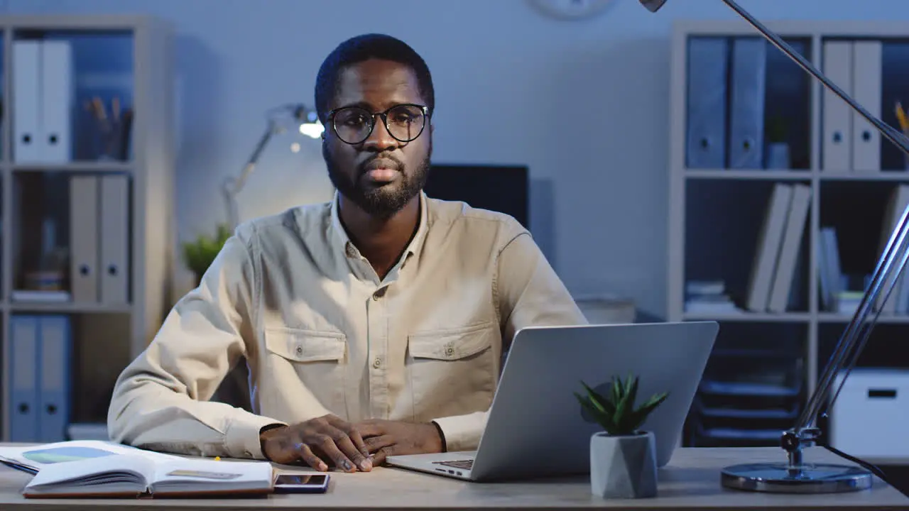 Young Office Worker Sitting At The Office Desk Looking And Smiling At Camera In The Office At Night