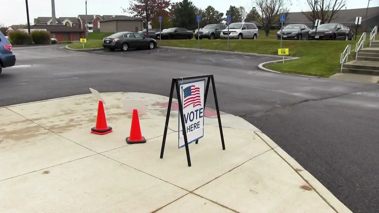 Vote here sign with American flag blowing in the wind wide