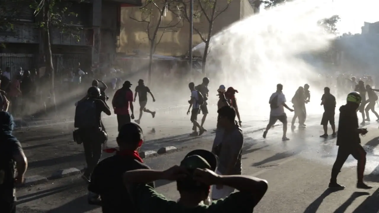 Armored riot police vehicle uses fire hose to spray water and scatter rioters