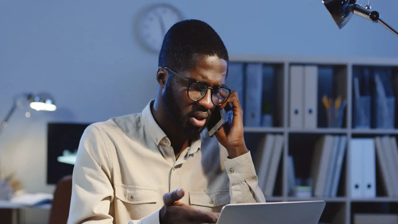 Portrait Of Young Office Worker Sitting At Desk And Talking On The Phone In The Office At Night