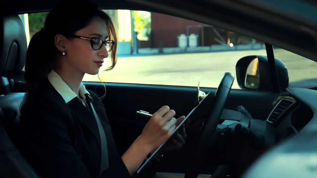 Attractive caucasian business woman in a parked car writing down notes on a clipboard while concentrating and thinking