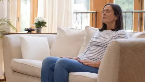 Pull Focus Shot of Middle Aged Woman Meditating On Sofa