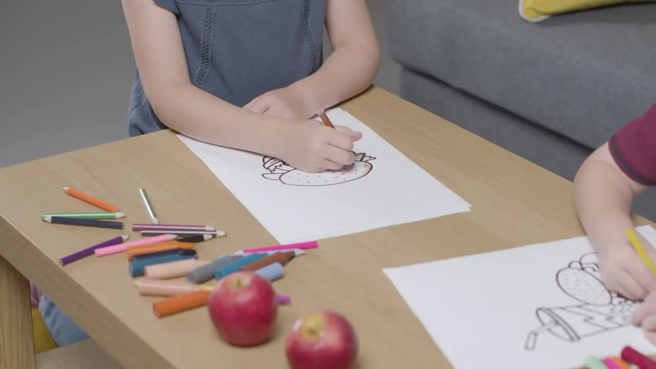 Close Up Of Two Children At Home Colouring In Picture At Table