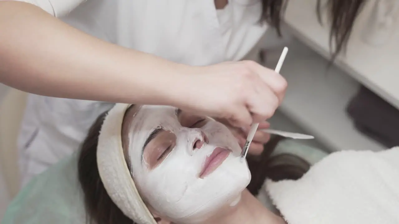 Professional cosmetician applying face mask to a customer