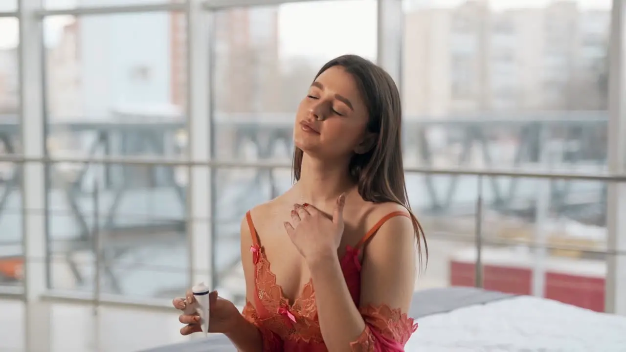 Pretty girl applies cream on the skin while sitting on the bed in the bedroom