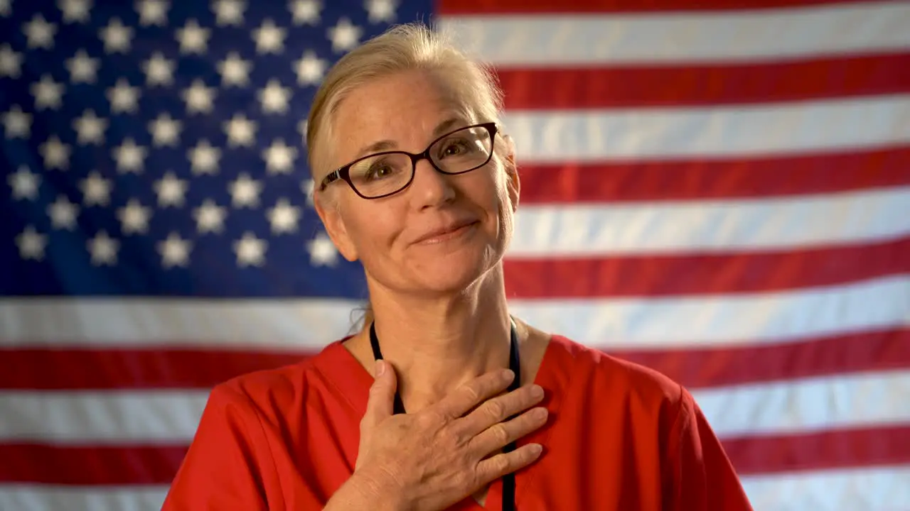 Medium tight portrait of a healthcare nurse looking happy and relieved with an out of focus American flag