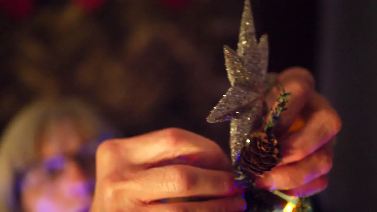 A woman hanging a sparkling star ornament on top of a Christmas tree during the holiday season