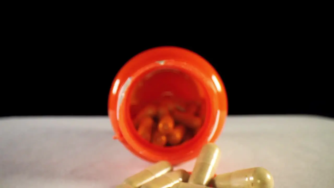 moving past capsules in cap pushing towards the opening of an orange supplement pill bottle