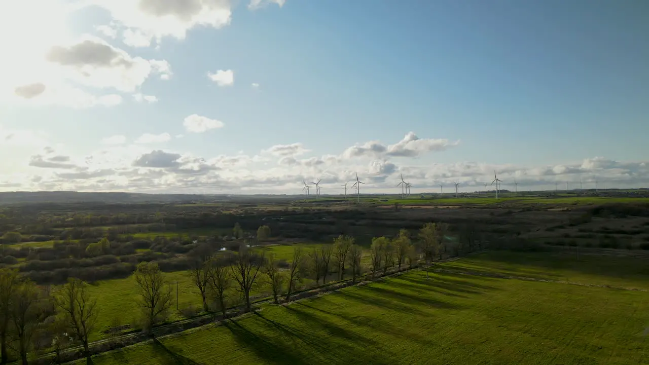 Aerial drone flies over green fields and line of trees in spring Windmill farm factory on background in Puck Poland on sunny and cloudy day