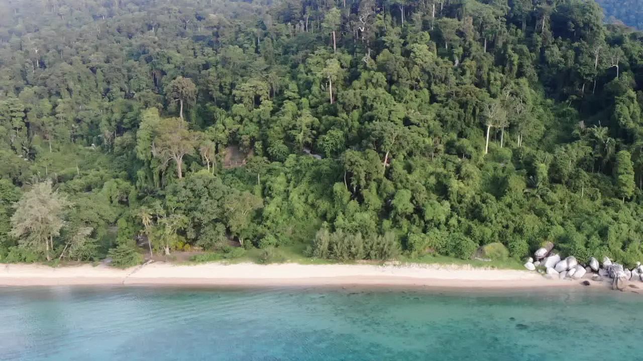 A drone video flying outward from an empty Tioman tropical island with full of trees and tropical forest toward a beautiful blue aquamarine ocean vitamin sea