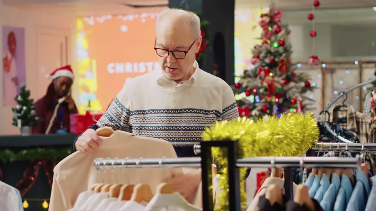 Tired elderly man browsing through clothes in festive fashion store looking for family gifts fed up with Christmas shopping Senior customer picking elegant blazer for nephew