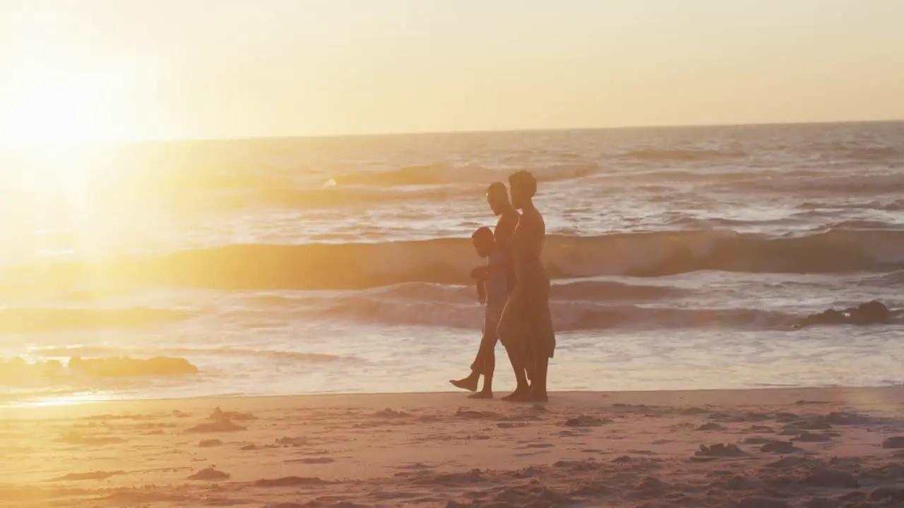 Video of happy african american family walking on beach at sunset