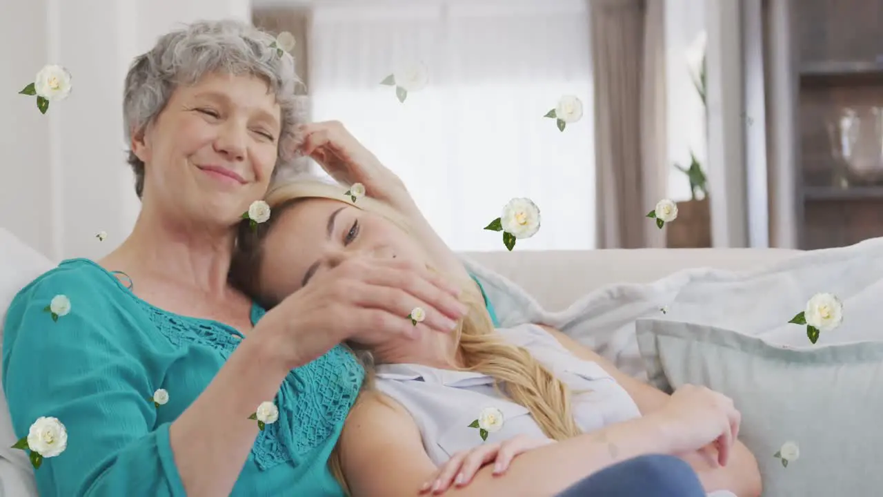 Animation of roses over happy caucasian mother and adult daughter hugging on sofa