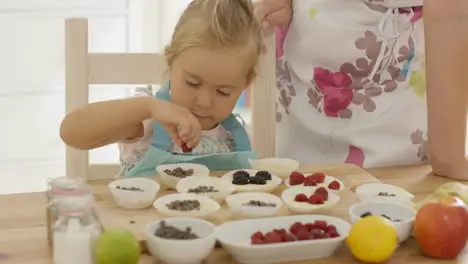 Little girl placing berries on muffins