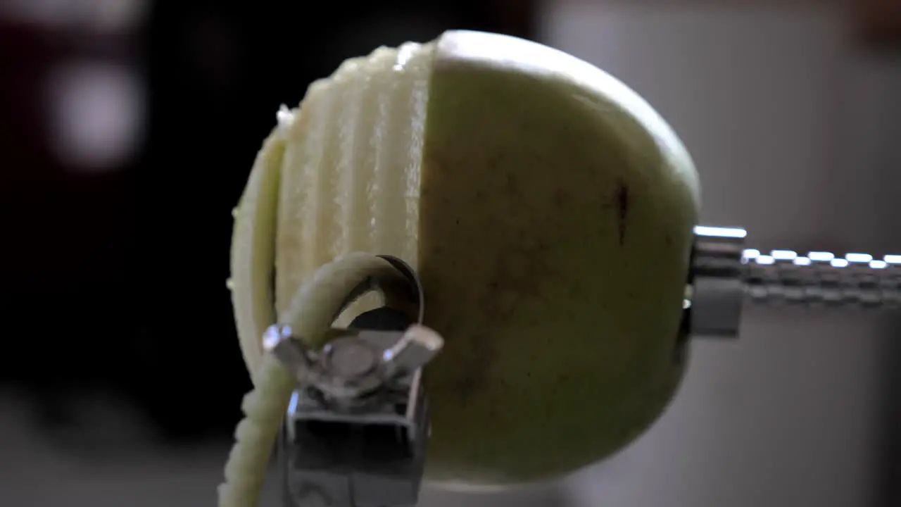 Side view of metal kitchen device peeling cutting and core green juicy apple skin and flesh on kitchen bench with juice flying out