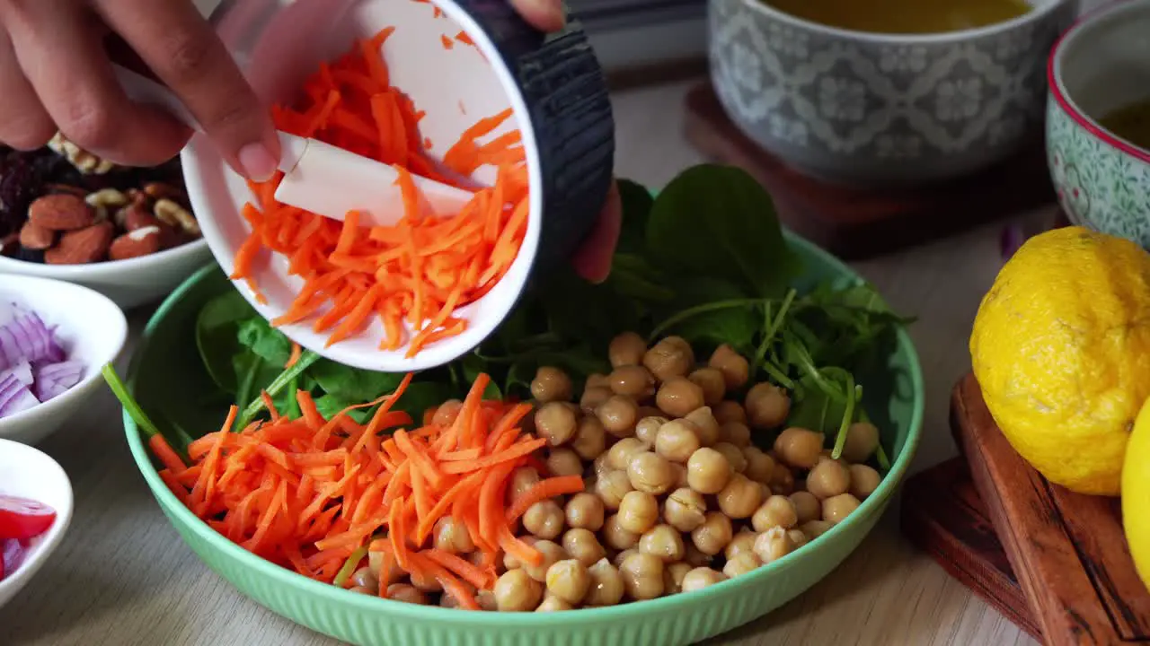 Handheld shot making of a salad adding carrots tomatoes spinach chick peas lemons onions nuts dressing in view