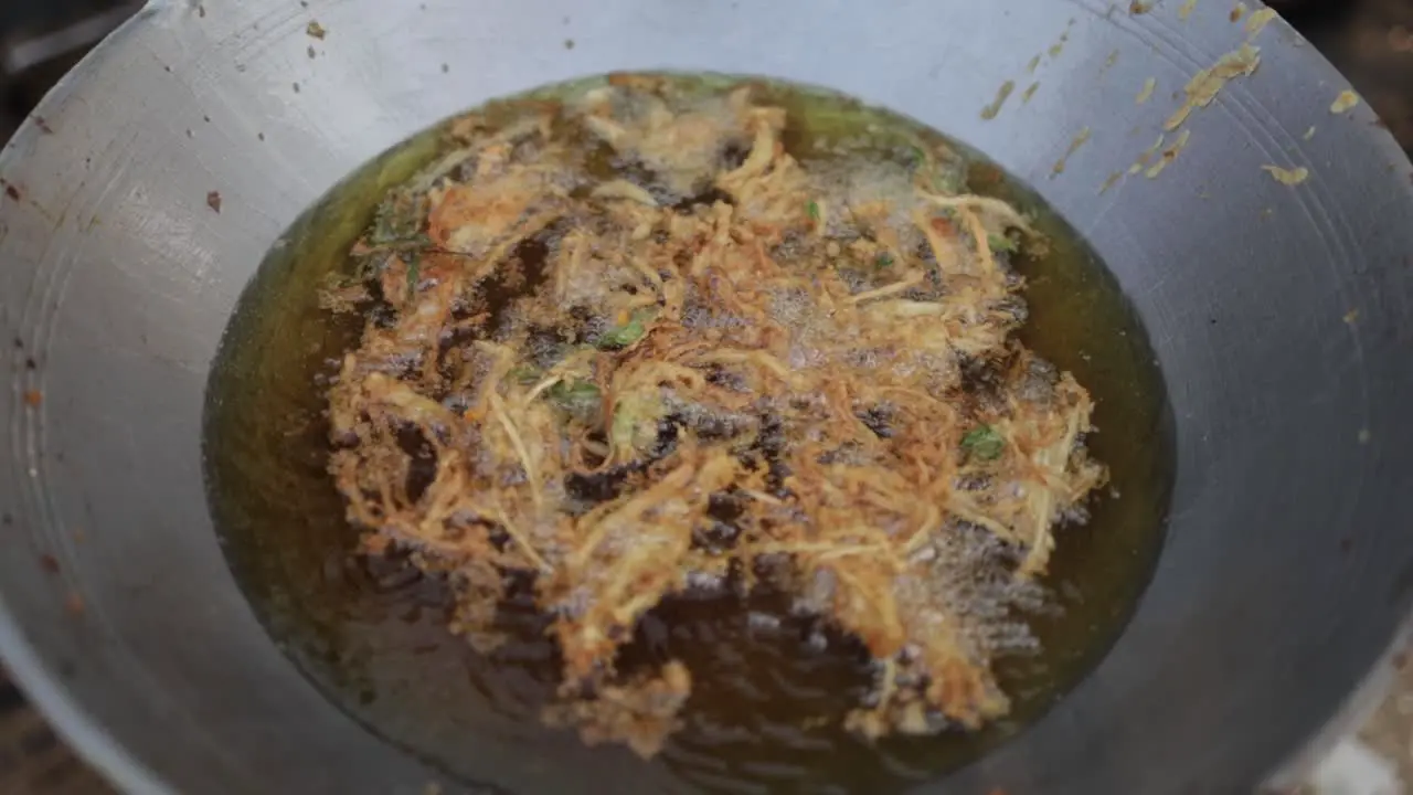 Top view of deep-fried Enoki Mushroom or Golden Needle Mushroom floating on hot boiling oil in big frying pan at food stall street market