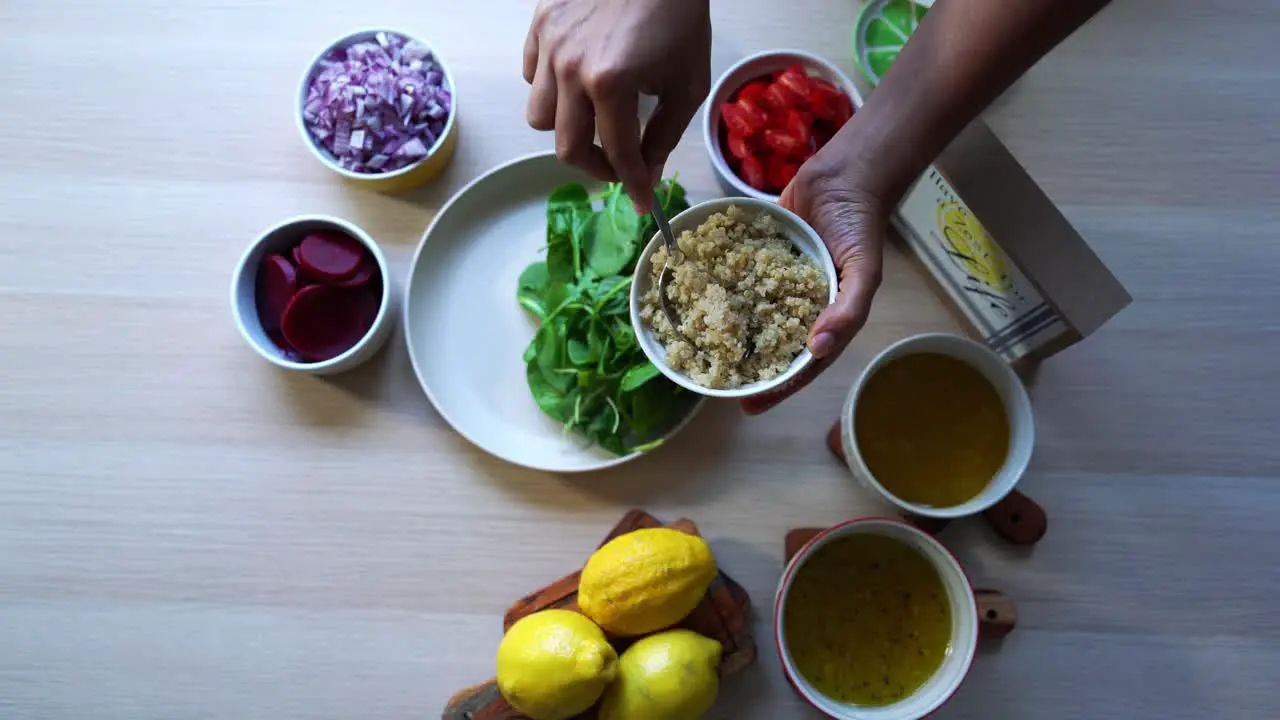 Aerial shot of Adding quinoa to plate of spinach salad making of a salad adding tomatoes carrots spinach chick peas lemons onions nuts dressing in view