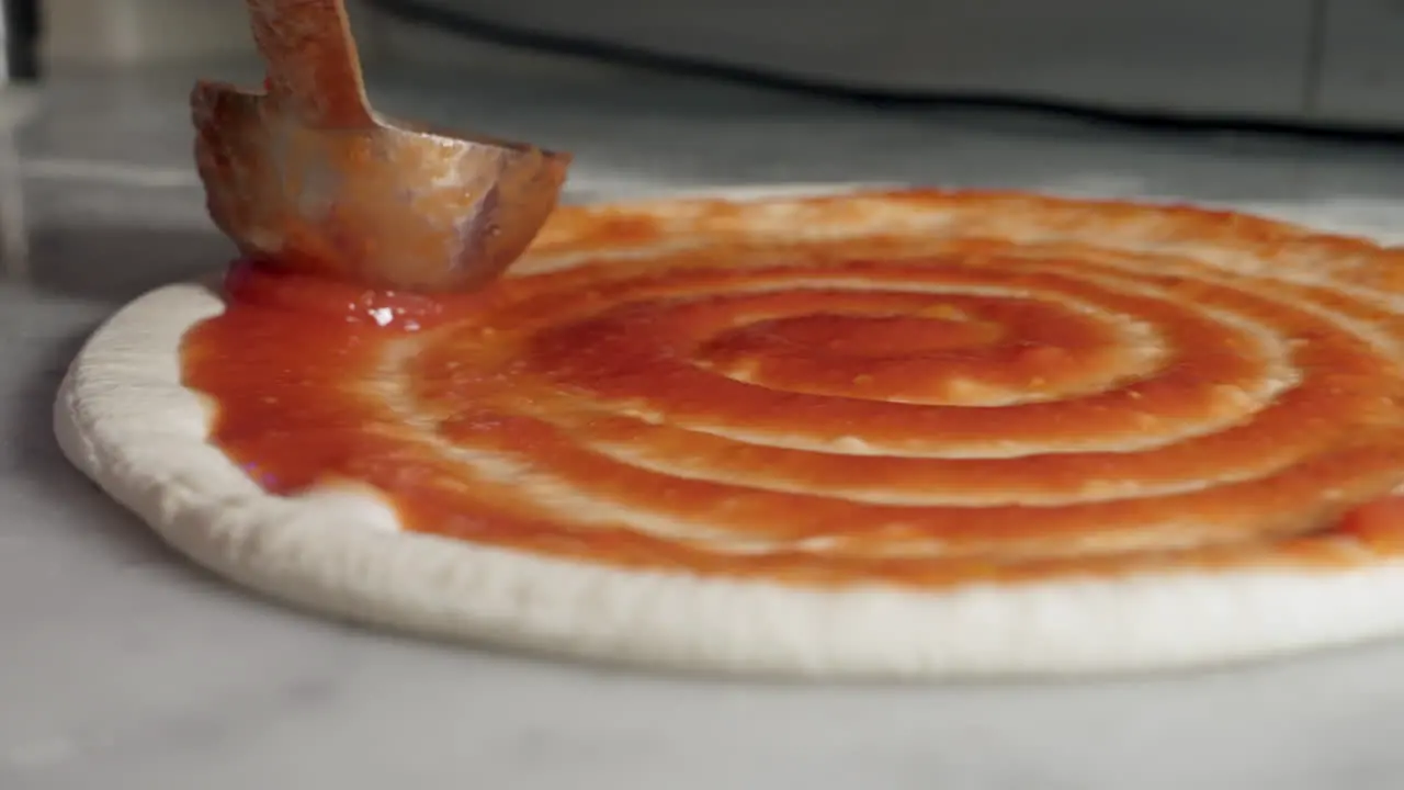 Tomato sauce being spread onto pizza base in a swirling motion close up shot