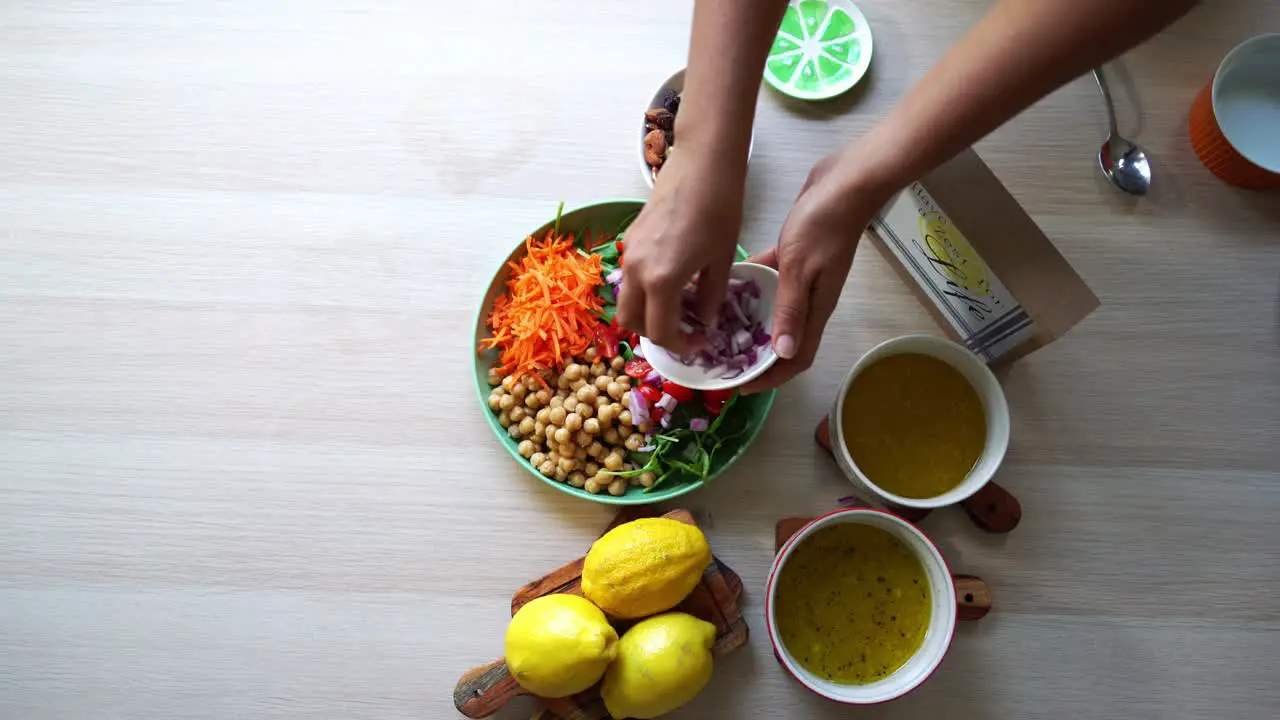 Aerial shot making of a salad adding tomatoes carrots spinach chick pease lemons onions nuts dressing in view