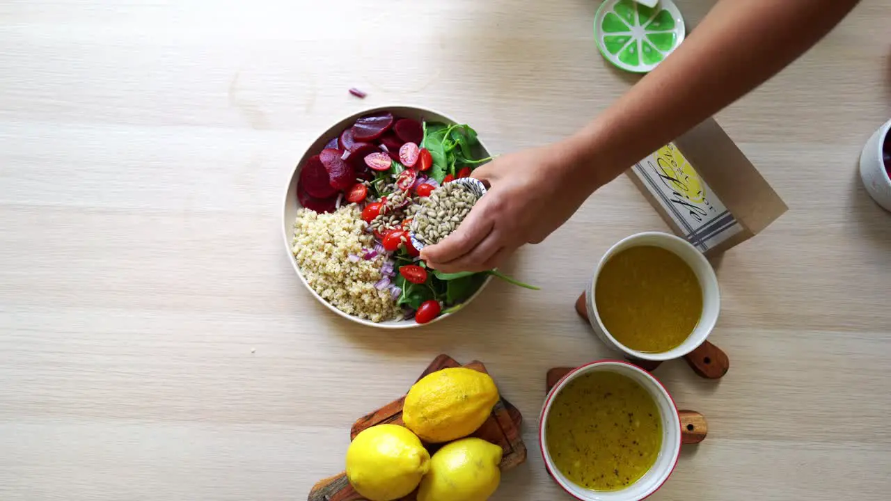 Adding seeds to salad spinach to dish beets quinoa seeds lemons and onions in the scene tomatoes and salad dressing