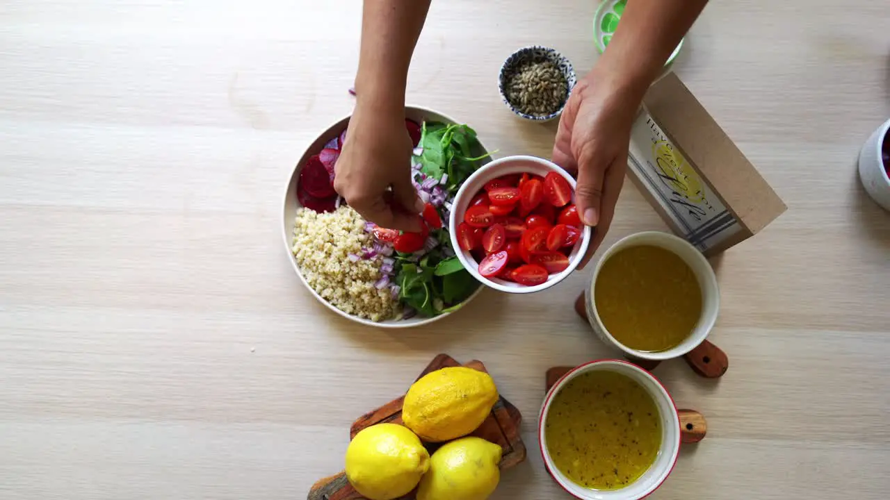 Adding tomatoes to salad dish beets quinoa seeds lemons and onions in the scene tomatoes and salad dressing