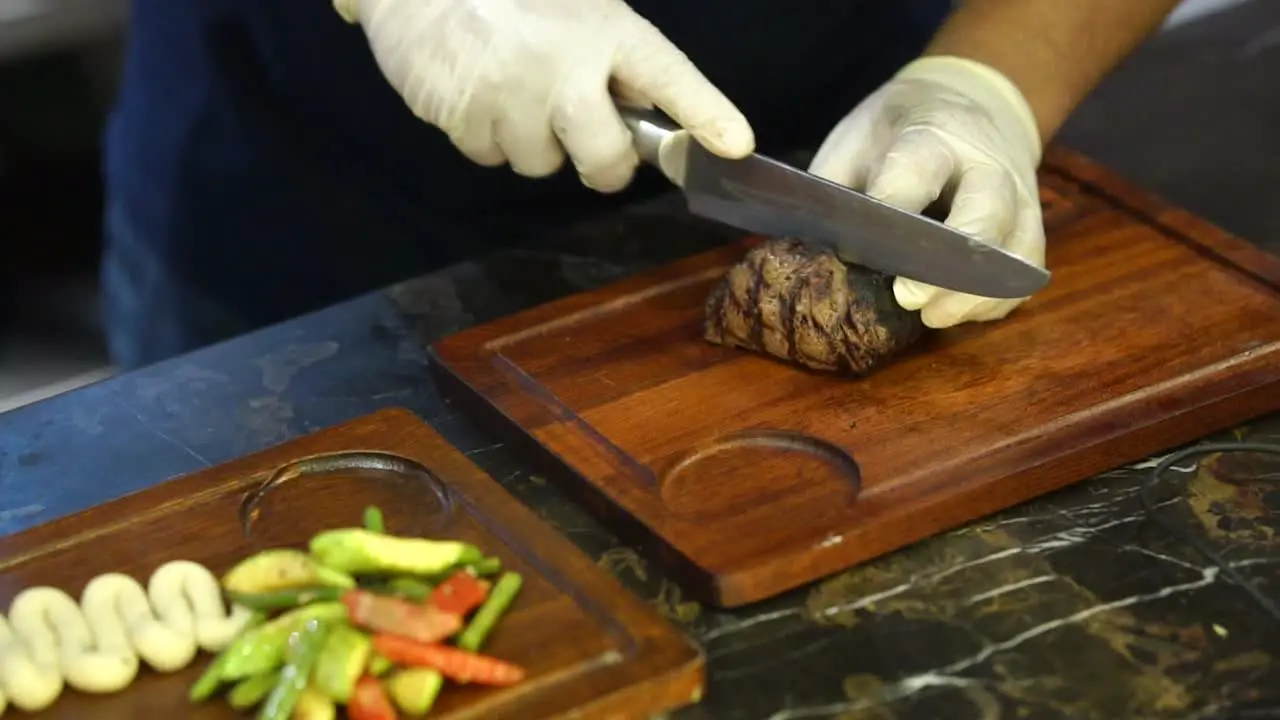 Up close chef with gloves cutting juicy piece of beef steak with sharp knife