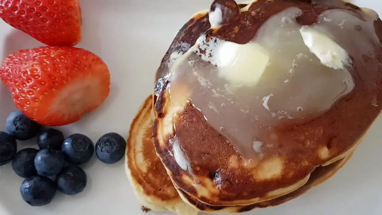 Over top zooming into pancakes with honey butter topping and strawberry and blueberries