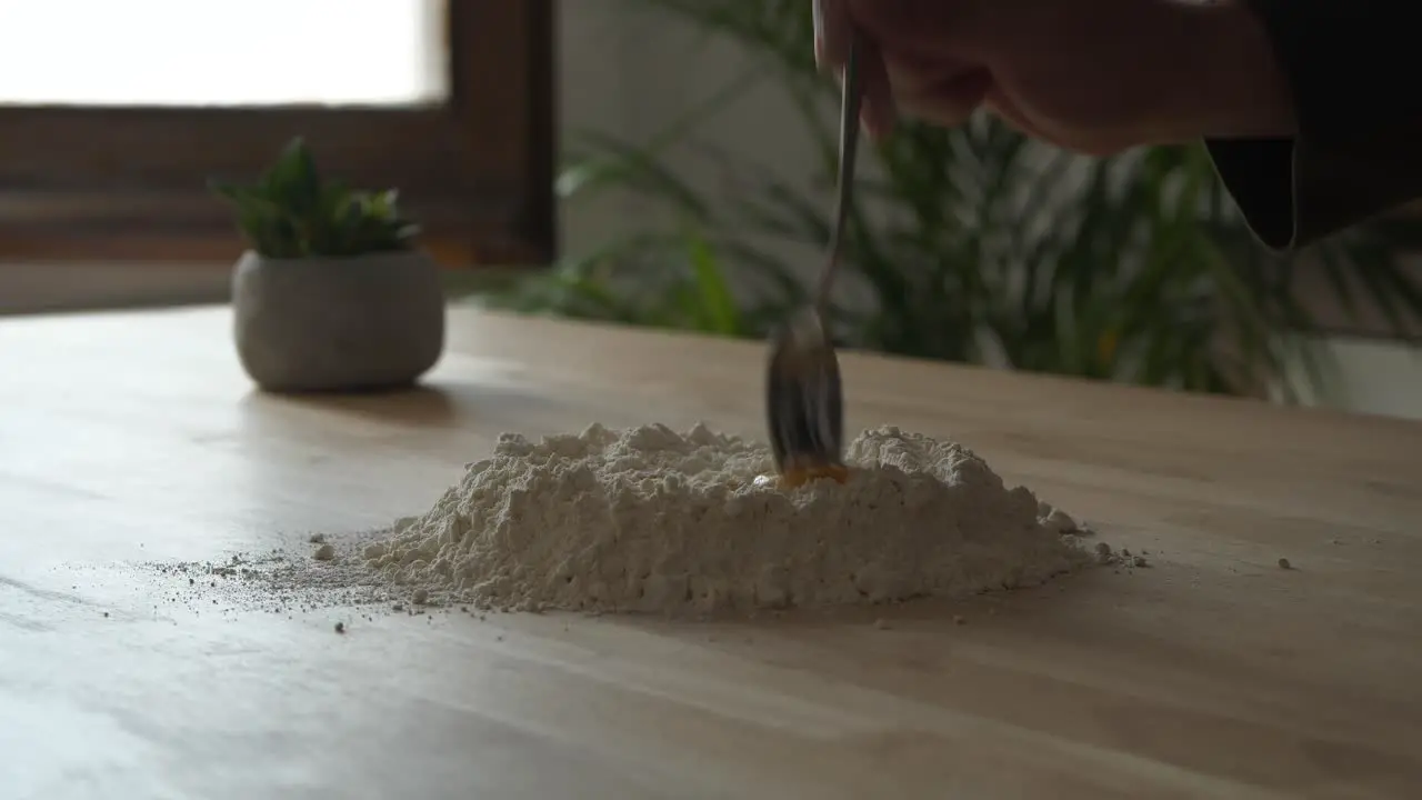 Person preparing mix blending flour and egg yolk on wooden kitchen table surface making fresh pasta dough