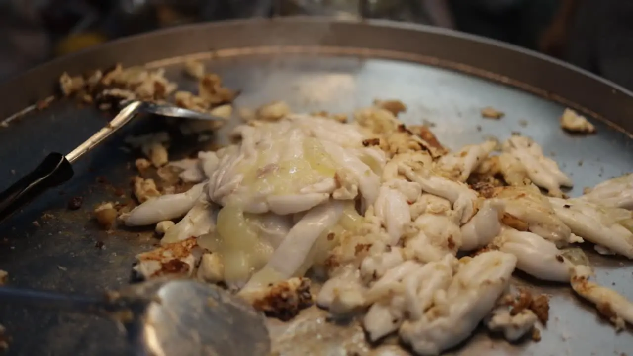 Close-up of pan-fried squid eggs in a smoking hot large frying pan at a hawker center