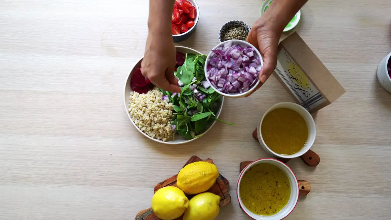 Adding onions Making a salad to dish beets quinoa seeds lemons and onions in the scene tomatoes and salad dressing