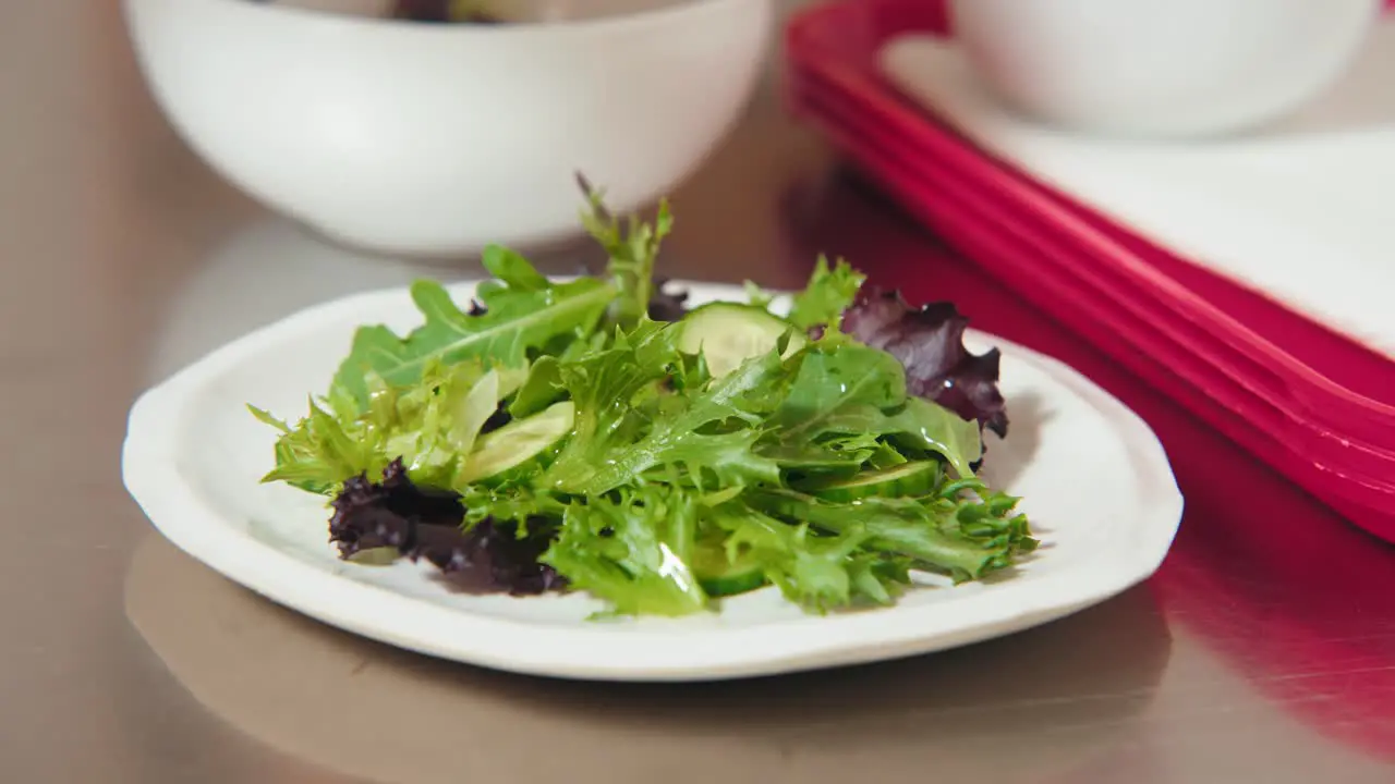 A Professional Chef Food Photographer Culinary artist Plating a Thin Shallot Slice on a Leafy Green Salad Bowl for a Food Photo with a Delicate Set of Tweezers in a Kitchen Workspace