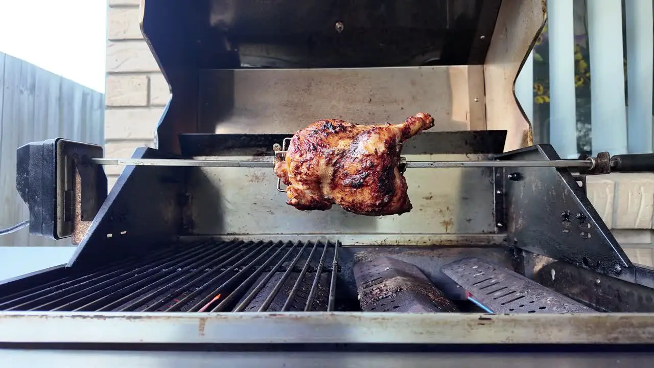 Opening of a BBQ hood to reveal a chicken being grilled on a rotisserie